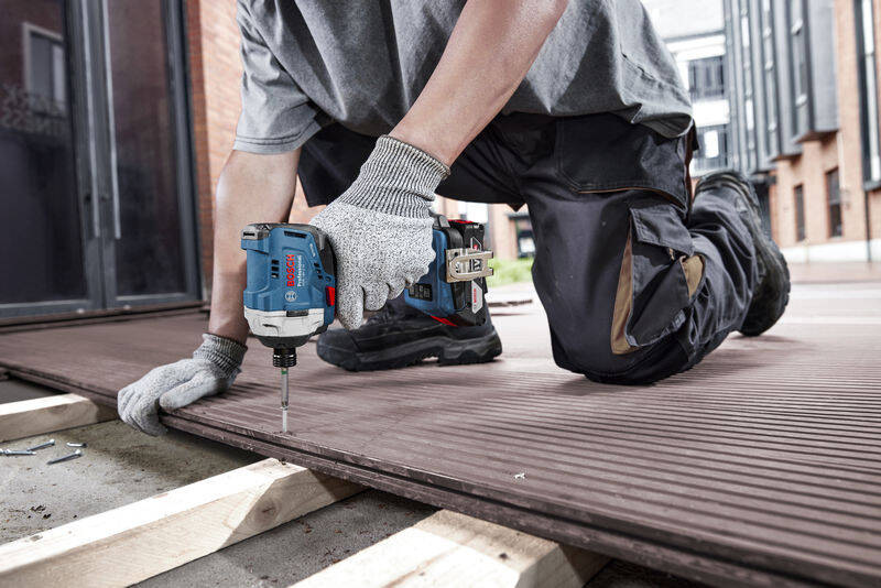 Utahovák rázový Bosch Professional GDR 18V-215 (bez baterie) Muž klečí na zemi na stavbě a vrtá s Rázovým utahovákem Bosch Professional GDR 18V-215
