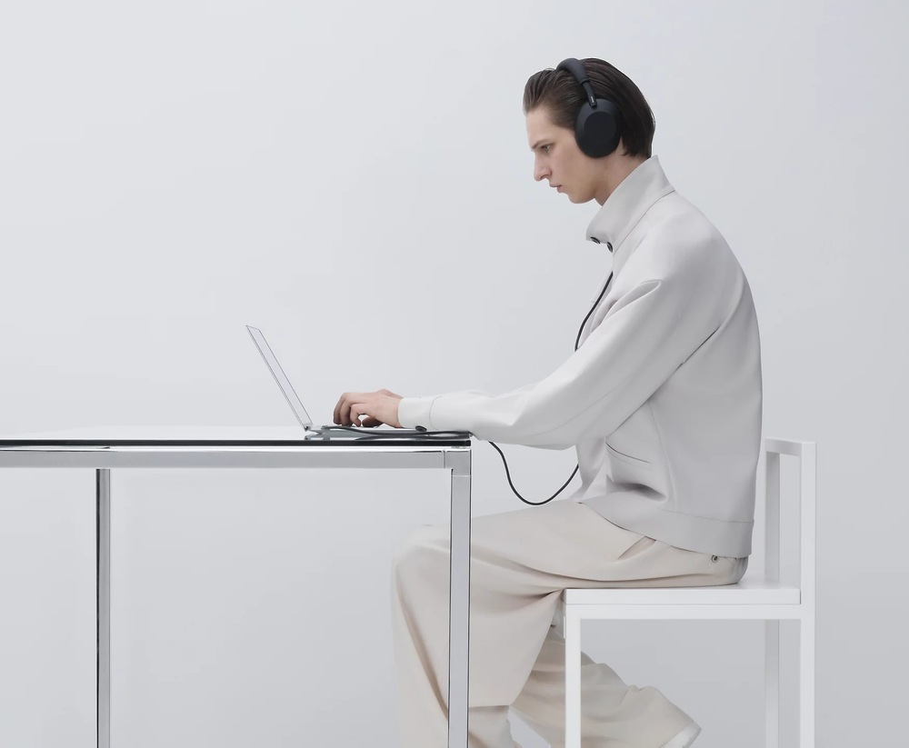 Sluchátka Sony WH-1000XM6, Noise Cancelling - Prodloužená záruka zdarma po registraci růžová Muž sedící u stolu pracuje na notebooku, k němuž má kabelem připojená sluchátka Sony WH-1000XM6