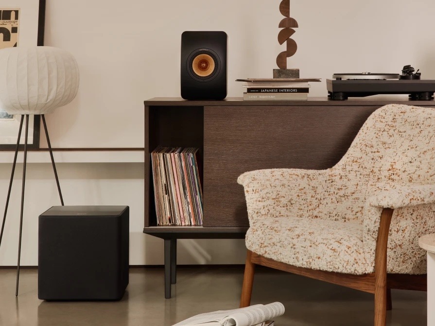Subwoofer KEF Kube 10 MIE (1 ks) černý Černý subwoofer KEF Kube 10 MIE na podlaze v obývacím pokoji vedle skříňky s gramofonem, reproduktorem KEF a vinylovými deskami.