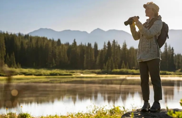 Dalekohled Nikon Action 10×50 černý žena stojí s dalekohledem Nikon Action 10×50 v ruce na břehu řeky, kolem ní se rozprostírá úchvatná příroda.