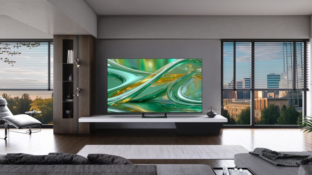 televize Hisense 55E8S v moderním pokoji. Na TV je zelené pozadí, v pokojí je křeslo, gauč, stolek a velká okna s výhledem