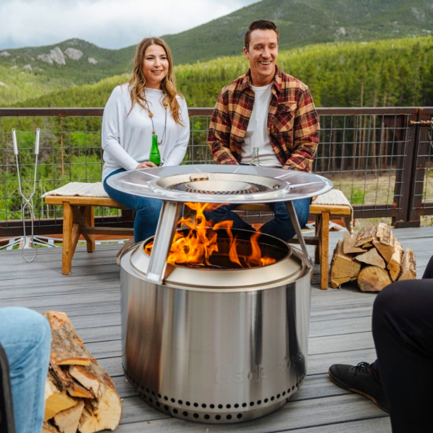Lidé sedí kolem ohniště Solo Stove Yukon s deflektorem tepla při večerním posezení na terase
