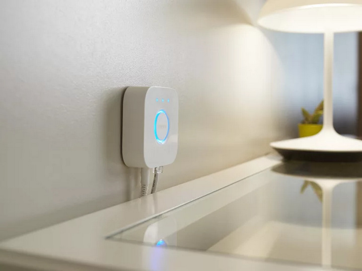 Ovladač Philips Hue Bridge 2.0 umístěný na zdi nad stolkem.