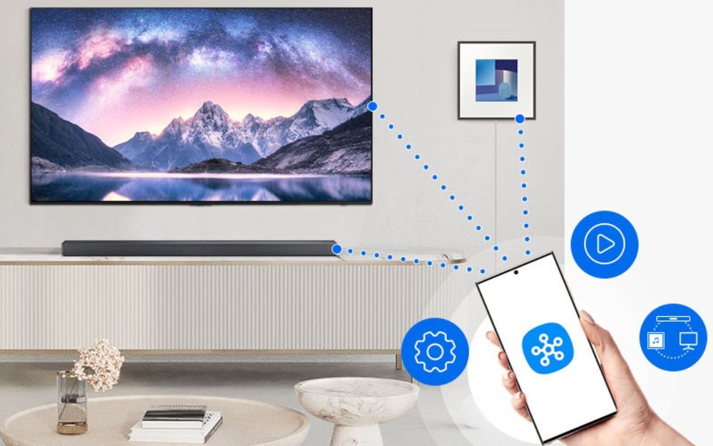 Soundbar Samsung HW-Q600H černý Soundbar Samsung je možné ovládat i přes mobilni aplikaci. Z telefonu vychází puntíky k televizi a soundbaru. Televize visí na zdi a pod ní je soundbar na stolku.