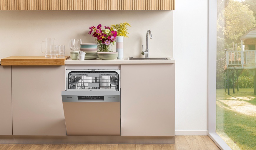 Vestavná myčka Gorenje GI643C90X je zabudovaná v kuchyňské lince. Její dvířka jsou pootevřená a na lince je váza s květinami.