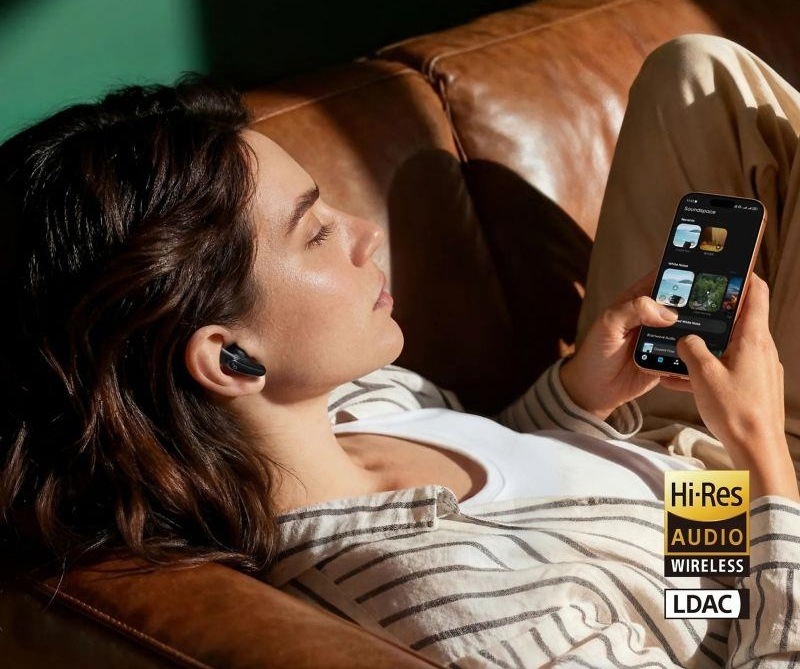 Žena se sluchátky Soundcore Liberty Buds drží v ruce smartphone s hudební aplikací