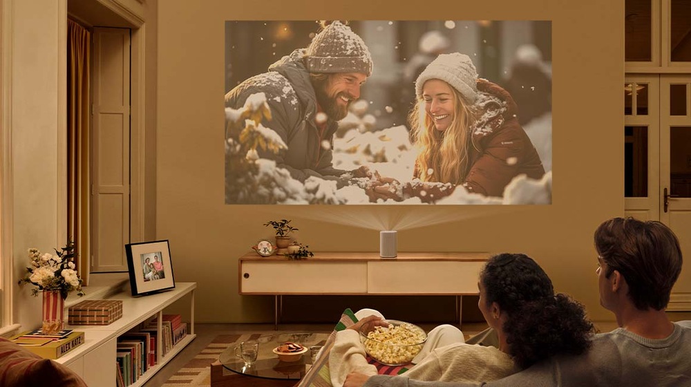 Laser TV Samsung SP-LPF5DSA Dva lidé sedí v obývacím pokoji a sledují film promítaný projektorem The Premiere 5 na zeď