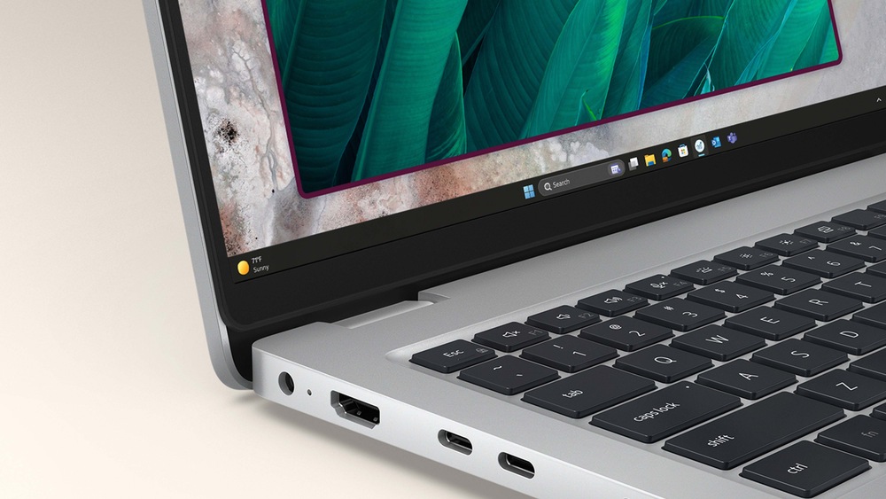 Detailní záběr na částečně otevřený elegantní notebook zobrazující živou zelenou tapetu s motivem listů. Důraz je kladen na klávesnici, porty HDMI a USB-C, které symbolizují moderní technologii.