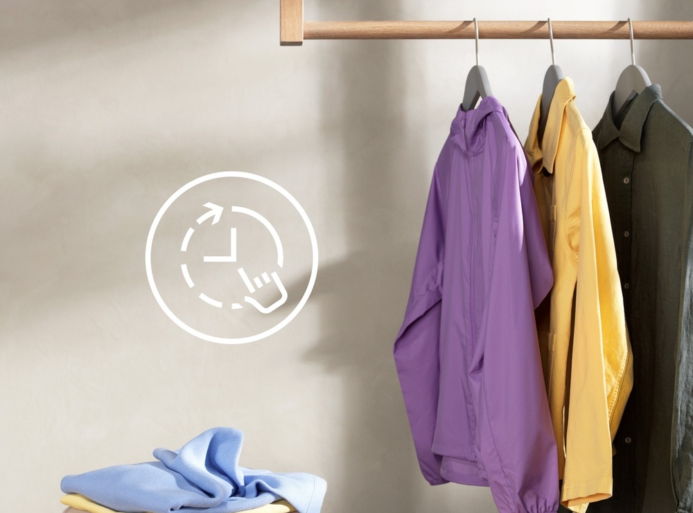 Na ramínku visí fialová bunda, žlutá a khaki košile. Vlevo symbol pro funkci TimeManager.