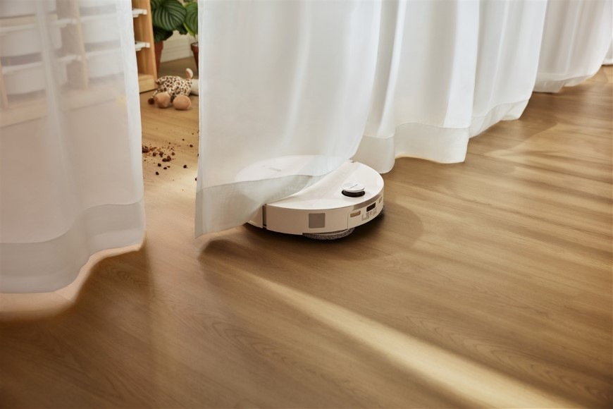 Robotický vysavač Roborock Qrevo Edge 2 White bílý Vysavač Qrevo Edge 2 projíždí pod záclonami do další části místnosti s vysypaným nepořádkem