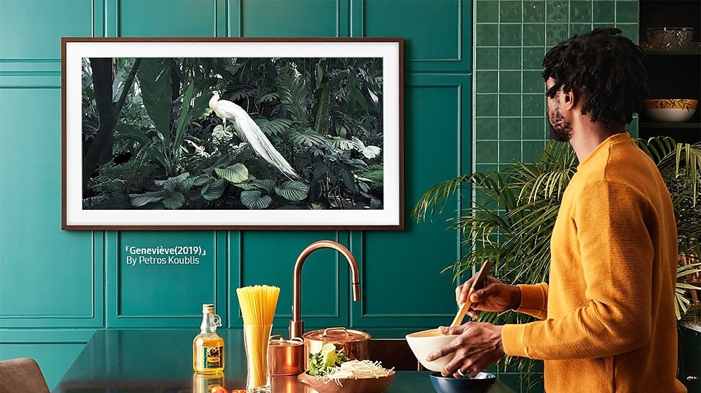 Výměnný rámeček Samsung pro Frame TV s úhlopříčkou 50" (2021), Rovný design bílý Muž chystá jídlo a přitom se dívá na umělecké dílo zobrazené na televizi Samsung Frame zasazené do hnědého výměnného rámu