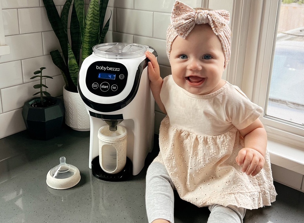 Ohřívač mléka Baby Brezza Formula Pro Mini je postavený na kuchyňské lince a vedle něho sedí usměvavé miminko.