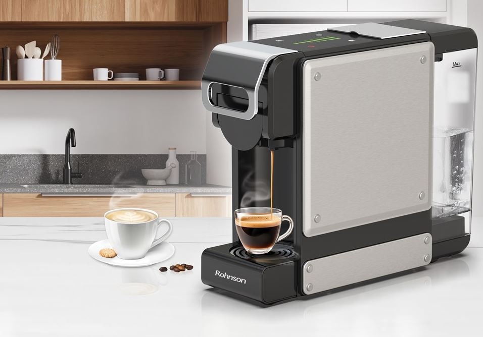 Kapslový kávovar Rohnson R-98054 černý/stříbrný kávovar Rohnson R-98054, který právě připravuje espresso. Vedle stojí již připravené cappuccino. Kávovar se nachází v dřevěno-bílé kuchyni.