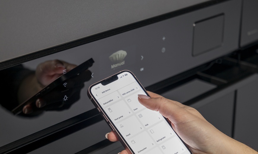 Trouba Hisense BFS615S8B černá Žena v ruce drží mobilní zařízení a v něm má otevřenou aplikaci ConnectLife. V pozadí je vestavná trouba Hisense BFS615S8B.