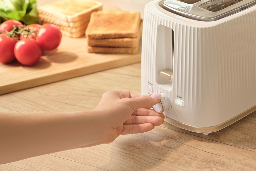 Topinkovač Sencor STS 7510WH bílý Žena otáčí knoflíkem intenzity opékání na topinkovači Sencor STS 7510WH. V pozadí jsou na prkénku položená rajčata a salát.