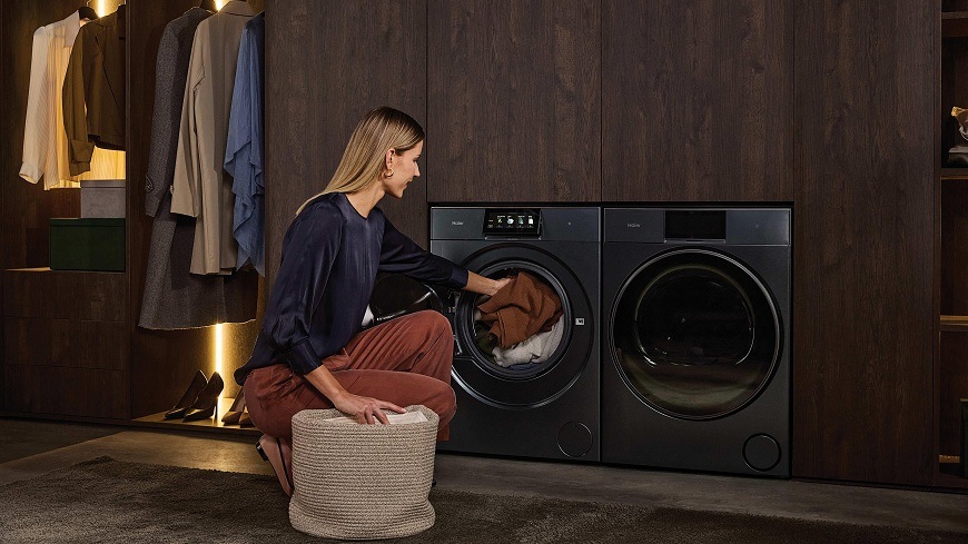 Pračka Haier HW100BD14L8GNU1S šedá žena v prádelně plní pračku Haier HW100BD14L8GNU1S prádlem