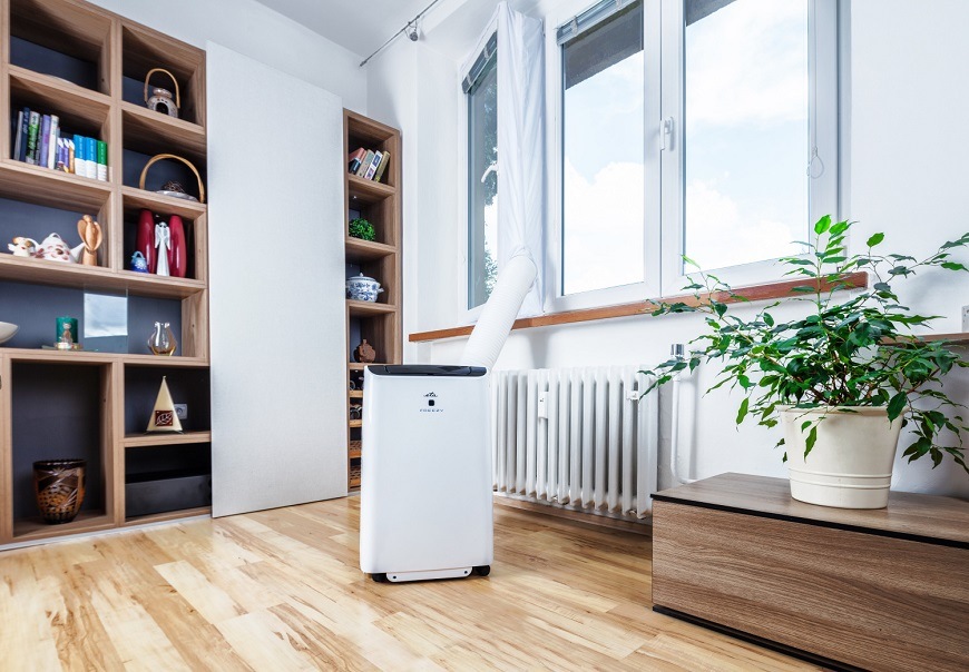 Okenní sada pro klimatizaci ETA Fresco 0578 90100 bílé Bílá mobilní klimatizace ETA Fresco s výfukovou hadicí ve světlém obývacím pokoji s dřevěnými parketami, policemi a květinou u okna