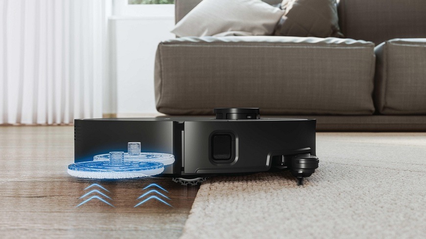 Robotický vysavač Hoover HG870HU 011 je zčásti na koberci a zčásti na podlaze, ze které při přechodu na koberec zvedá mopy