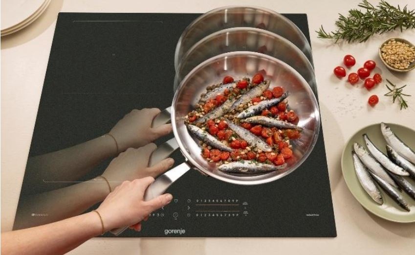 Indukční varná deska Gorenje G600 GI6442MSCWF InfiniteMatt černá Ruka přesouvá pánvicku s rybičkami z jedne varne zony na druhou.
