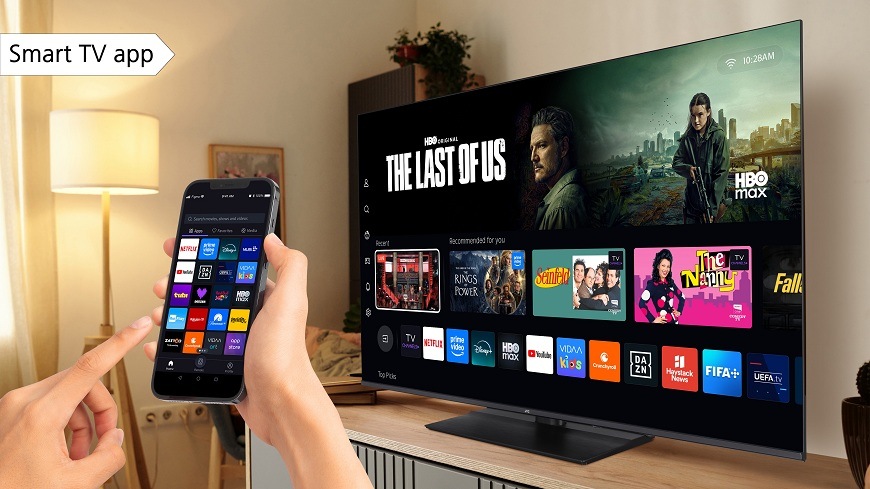 Televize JVC na dřevěném televizním stolku v obývacím pokoji zobrazující nabídku populárních seriálů, která je ovládána pomocí mobilního telefonu a aplikace VIDAA SMART TV