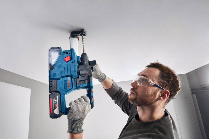 Muž v ochranných brýlích používá Vrtací kladivo Bosch Professional GBH 18V-18 pro vyvrtání děr ve stropu.