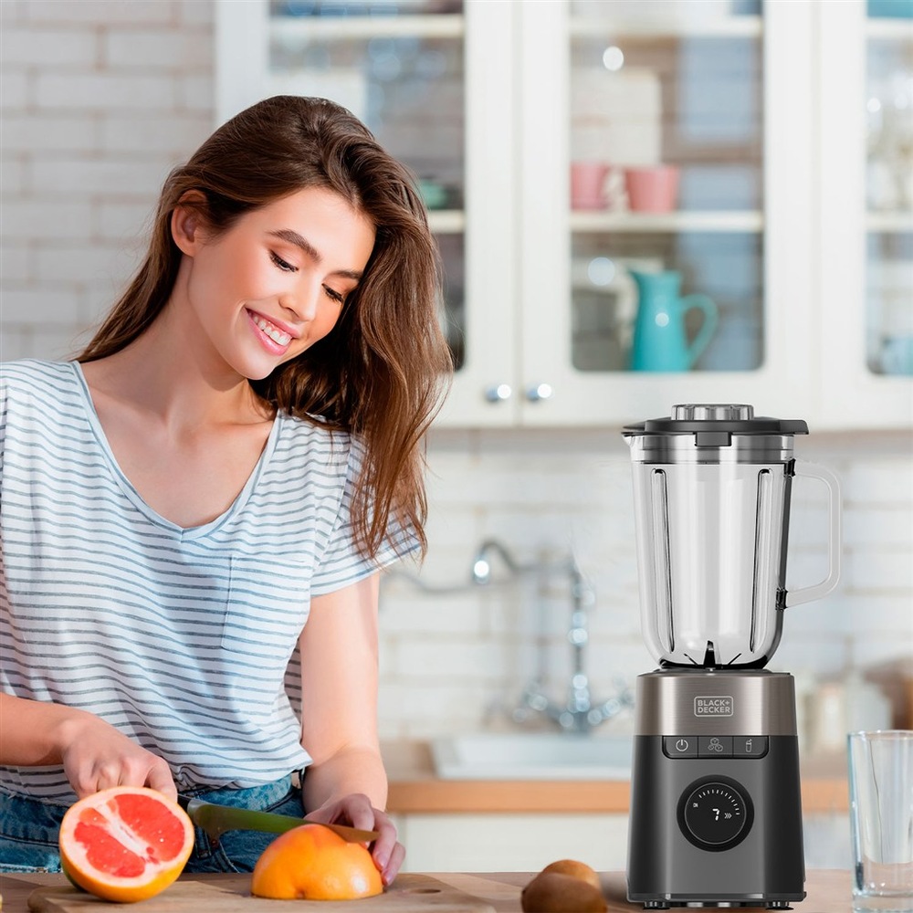 Stolní mixér Black+Decker BXJB1201E černý Žena krájí grapefruit v kuchyni vedle mixéru Black+Decker připraveného k použití.