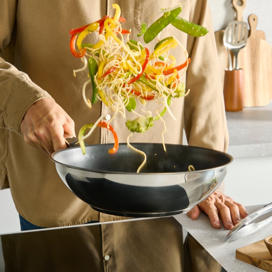 Pánev WOK Tefal Emotion+ E3271944, 28 cm nerez Muž připravující zeleninu ve wok pánvi Tefal E3271944 Emotion+ 28 cm.