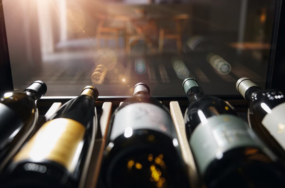 Vinotéka Miele KWTS 4785 F černá Pohled z vinotéky Miele KWTS 4785 F ven přes pět lahví vína, přes prosklená dvířka svítí slunce