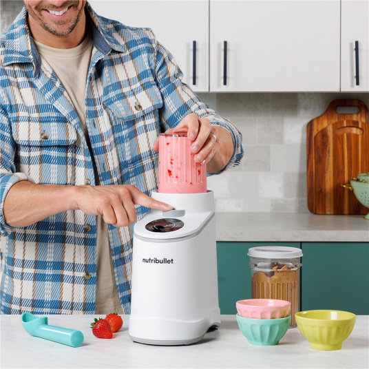 Muž obsluhující Nutribullet zmrzlinovač v kuchyni, vkládání nástavce s jahodovým smoothie.
