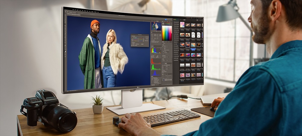 Muž upravuje módní fotografii dvou modelek na velké obrazovce počítače v moderní kanceláři. Na dřevěném stole je fotoaparát, který vyjadřuje kreativitu.