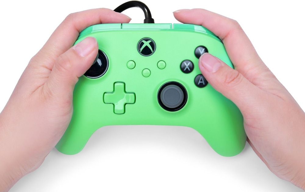 Gamepad PowerA Advantage Plus - Xbox zelený Na obrázku drží člověk oběma rukama herní ovladač PowerA Advantage Plus během hraní. Palce spočívají na analogových páčkách a tlačítkách, což ukazuje běžný způsob ovládání her. Dobře jsou vidět tlačítka A, B, X a Y, směrový kříž, funkční tlačítka uprostřed i tlačítko s logem Xbox. Snímek demonstruje ergonomický tvar ovladače, díky kterému pohodlně padne do rukou i při delším hraní.