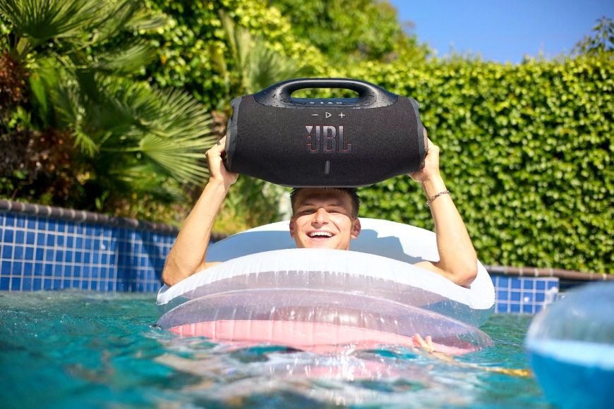 Přenosný reproduktor JBL Boombox 4 černý Muž drží Přenosný reproduktor JBL Boombox 4 v bazéně
