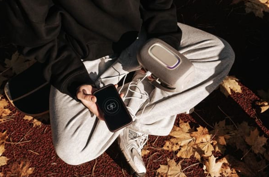 Mladý muž dobíjí mobilní telefon ze šedého reproduktoru Concept SoundJoy BR5021 v parku