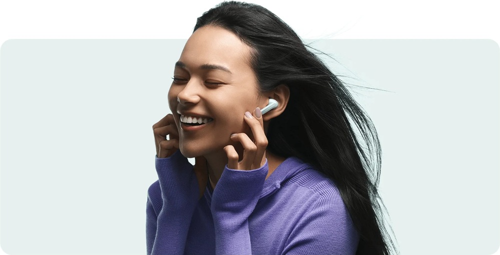 Sluchátka Xiaomi Buds 6 Nebula Purple fialová Smějící se žena s vlajícími vlasy od větru se sluchátky Xiaomi Buds 6 vybavenými redukci šumu při foukání větru