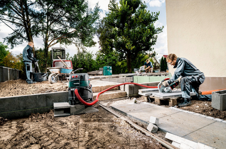 Pracovník řeže betonové dlaždice úhlovou bruskou Metabo při venkovních stavebních úpravách