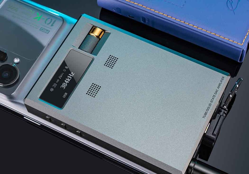 Elegantní audio zesilovač s digitálním displejem ukazuje „384 kHz“ a je připojen k chytrému telefonu. Poblíž leží modrý notebook, který vytváří technologicky zaměřenou atmosféru.