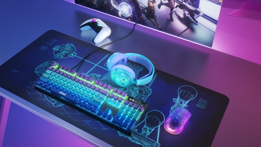 Podložka pod klávesnici a myš SteelSeries QcK XXL Fortnite modrá Podložka QcK XXL Battle Bus na stole s klávesnicí, myší a headsetem z kolekce Fortnite