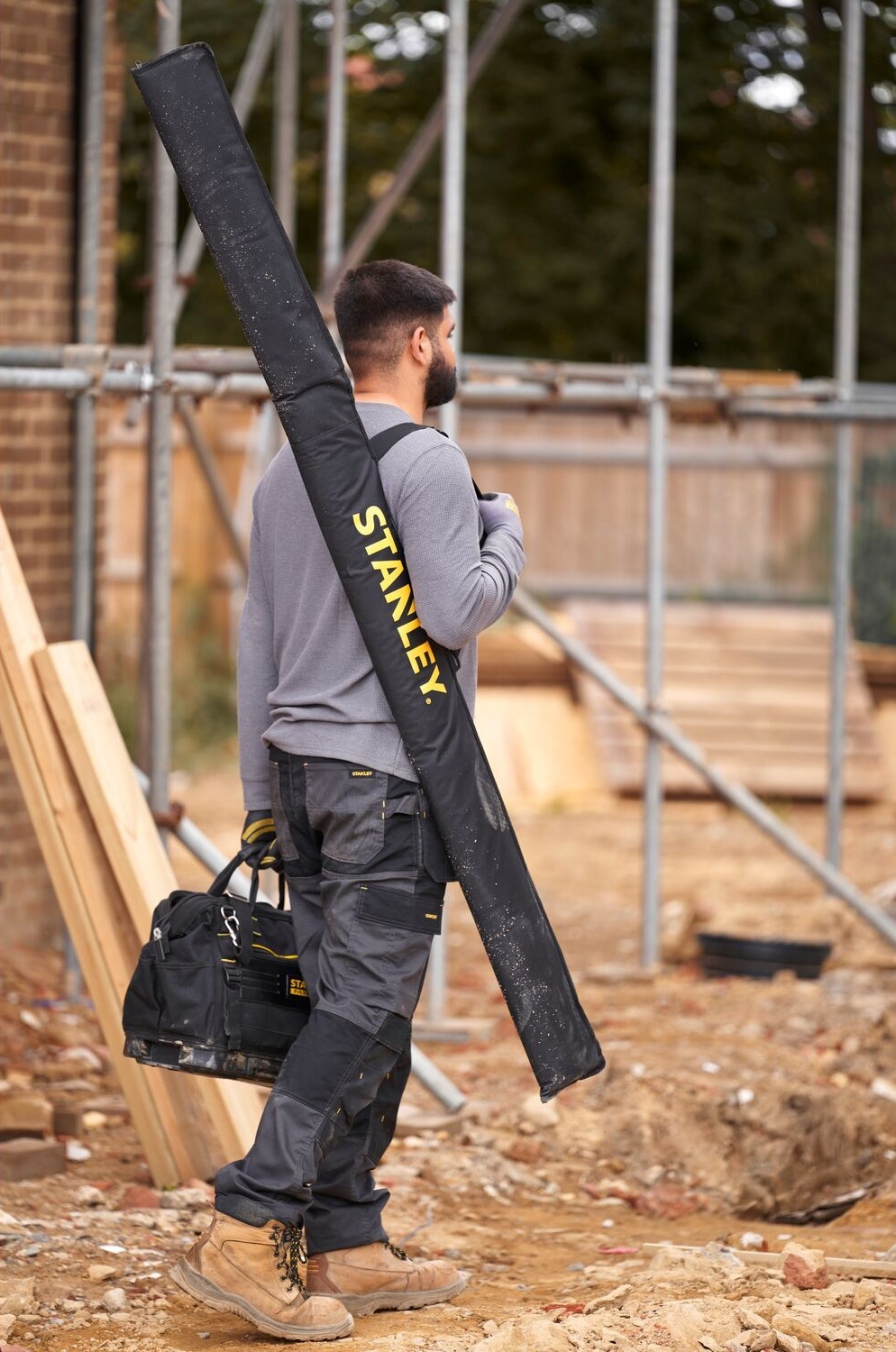 Brašna Stanley FatMax FMHT43685-1 Řemeslník nesoucí tašku Stanley na vodováhy přes rameno na staveništi.
