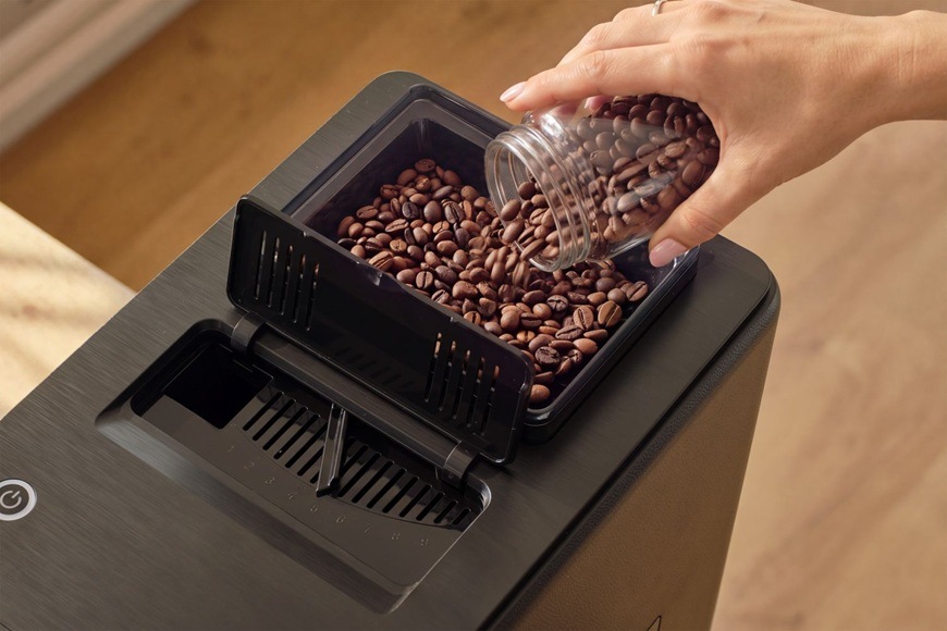 Automatický kávovar Sencor ENZO SES 9400BK Žena doplňuje zásobník kávovými zrny.