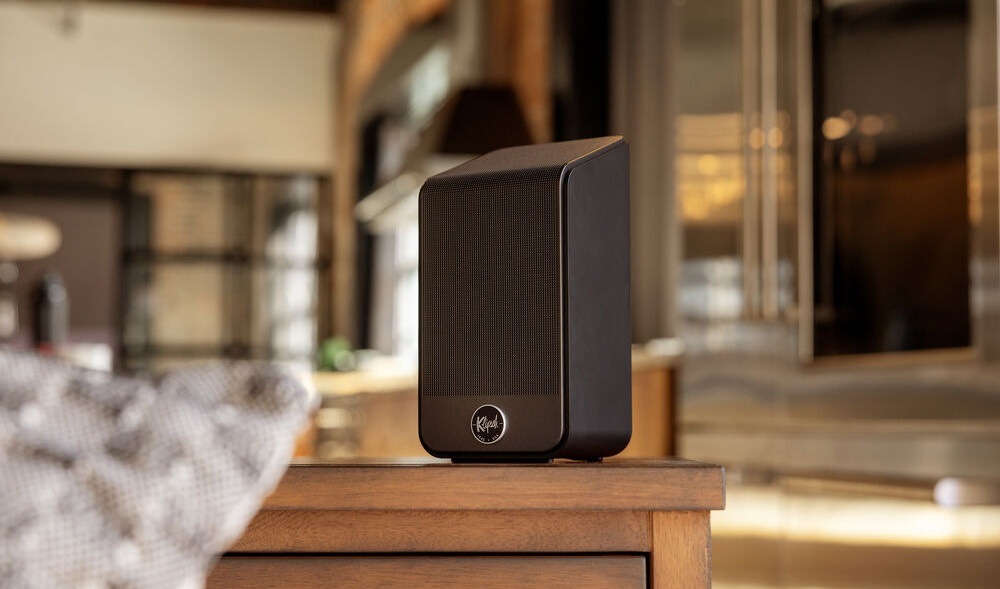 Reproduktory Klipsch Flexus SURR 200 (2 ks) černé Jeden reproduktor Klipsch Flexus SURR 200 stojí na stole, na pozadí je rozostřená místnost