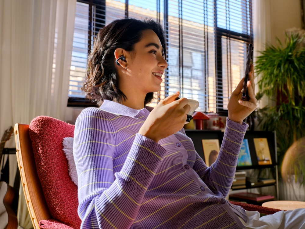 Sluchátka Shokz OpenDots Air, Bluetooth černá Žena se sluchátky Shokz při videohovoru a pití kávy