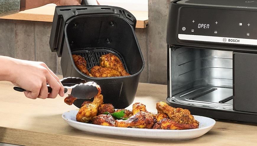 Fritéza horkovzdušná Bosch Serie 4 MAFD440B7 černá Ruka vytahující horké jídlo z horkovzdusné fritézy Bosch pomocí tepelně odolných kleští