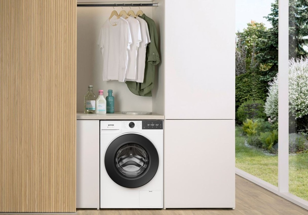 pračka Gorenje UltraClean zabudovaná do dřevěné skříňove stěny, nad pračkou visi trička na ramínku