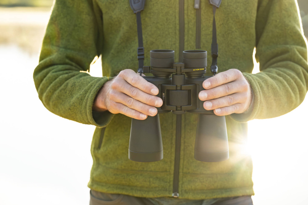 Dalekohled Nikon Action 12×50 černý Detailní pohled na dalekohled Nikon Action 12×50, který má muž v zelené mikině kolem krku.