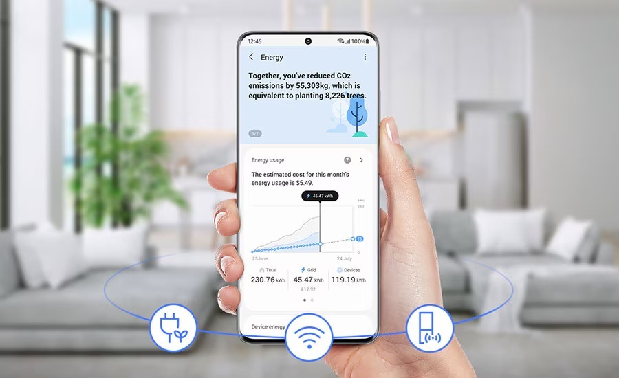 Americká lednice Samsung RF24BB620EB1EO černá Ruka drží mobilní telefon s aplikací SmartThings Energy, na pozadí je obývací pokoj