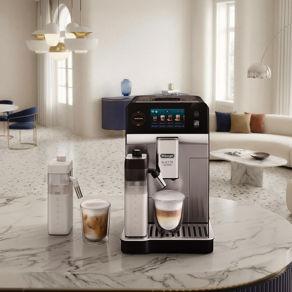 Ve světlém moderním obývacím pokoji stojí na mramorovém stole automatický kávovar De’Longhi vedle sklenic s pěnovým horkým a ledovým kávovým nápojem.