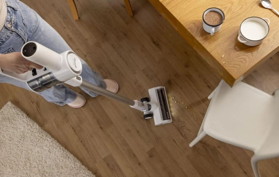 Tyčový vysavač Gorenje SVC216290FFW FreeForce bílý člověk vysává drobky vysavačem Gorenje SVC216290FFW s osvětlenou hubicí, vysává kolem stolu.