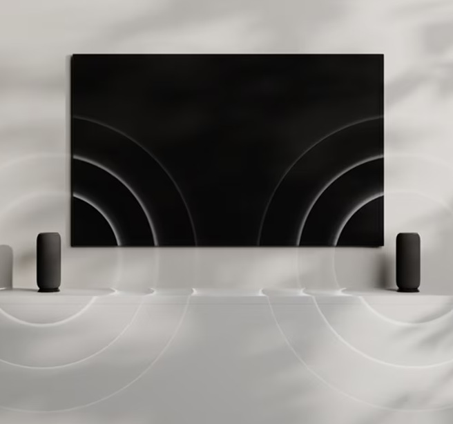 Dva propojené reproduktory Žena drží v ruce smartphone vedle reproduktoru Motorola Moto Sound Flow u televize