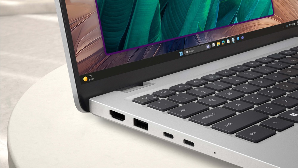 Elegantní notebook leží otevřený na světlém povrchu a na jeho zářivém displeji se zobrazují zelené listy. Stříbrné tělo je vybaveno porty USB a HDMI.
