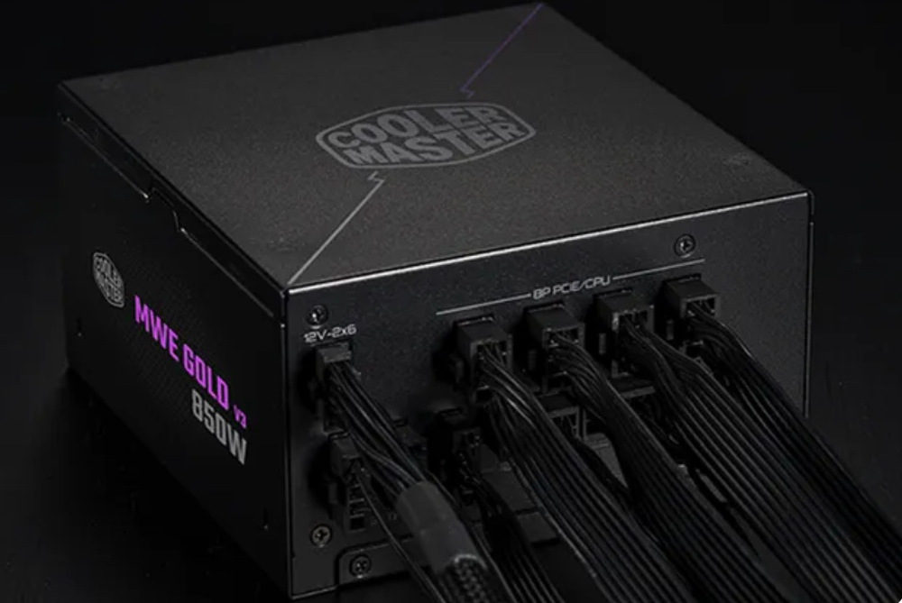 Na obrázku je černý napájecí zdroj Cooler Master s připojenými modulárními kabely. Je vidět zadní panel s osazenými konektory pro PCIe/CPU a další napájení, z nichž vystupují svazky černých kabelů. Na horní straně je logo Cooler Master a z boku nápis MWE Gold V3 850W.